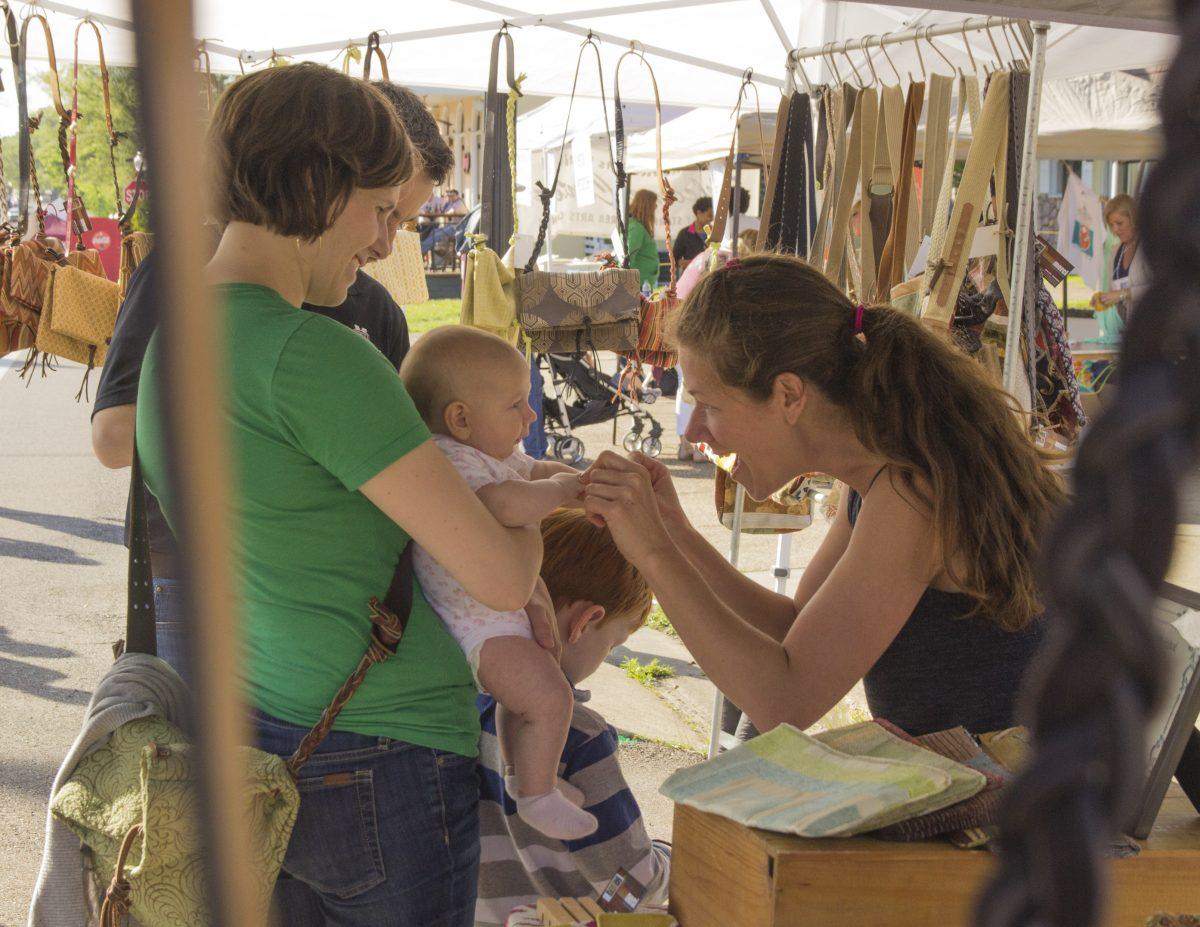 As the Cotton District Arts Festival comes to a close, a vendor momentarily plays with a customer’s child before packing up and heading home after the long day. 