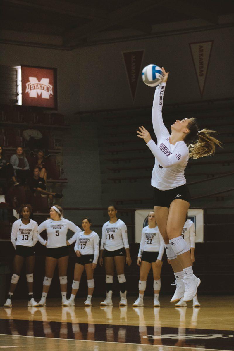 Callie Minshew serves the volleyball during the 2019 season as her teammates look on.