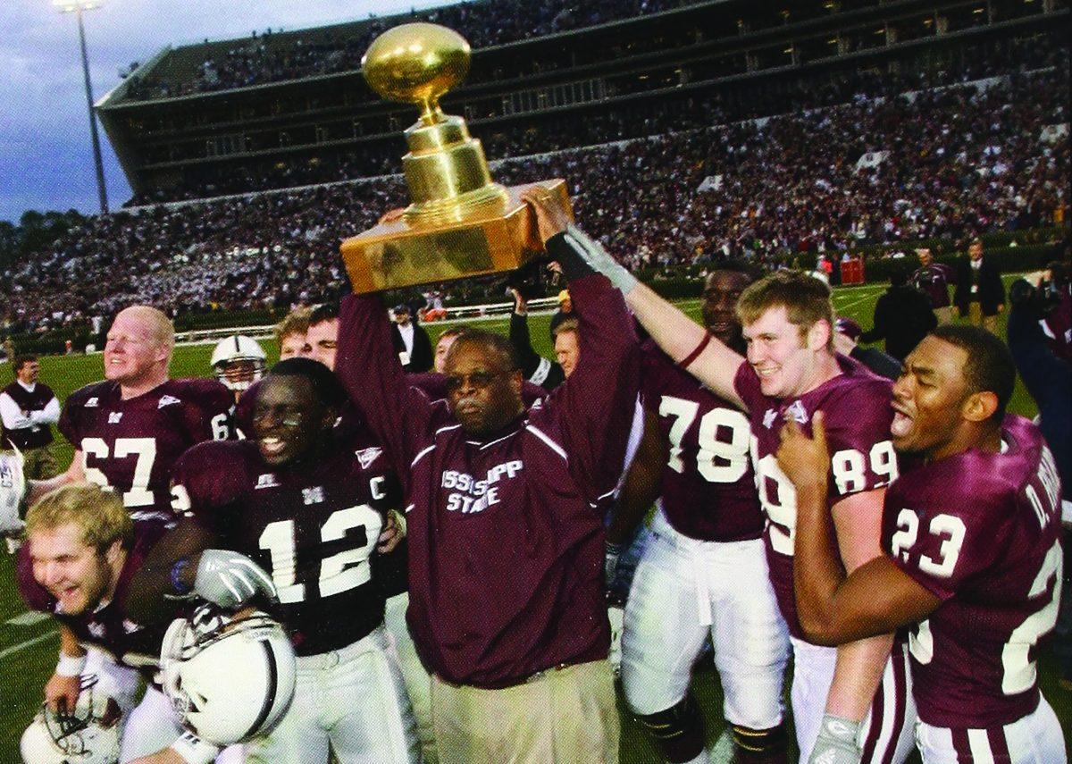 Former MSU football Head Coach Sylvester Croom hoists the Golden Egg after winning the Egg Bowl surrounded by a cheering team in a photo from The Reveille in 2005.