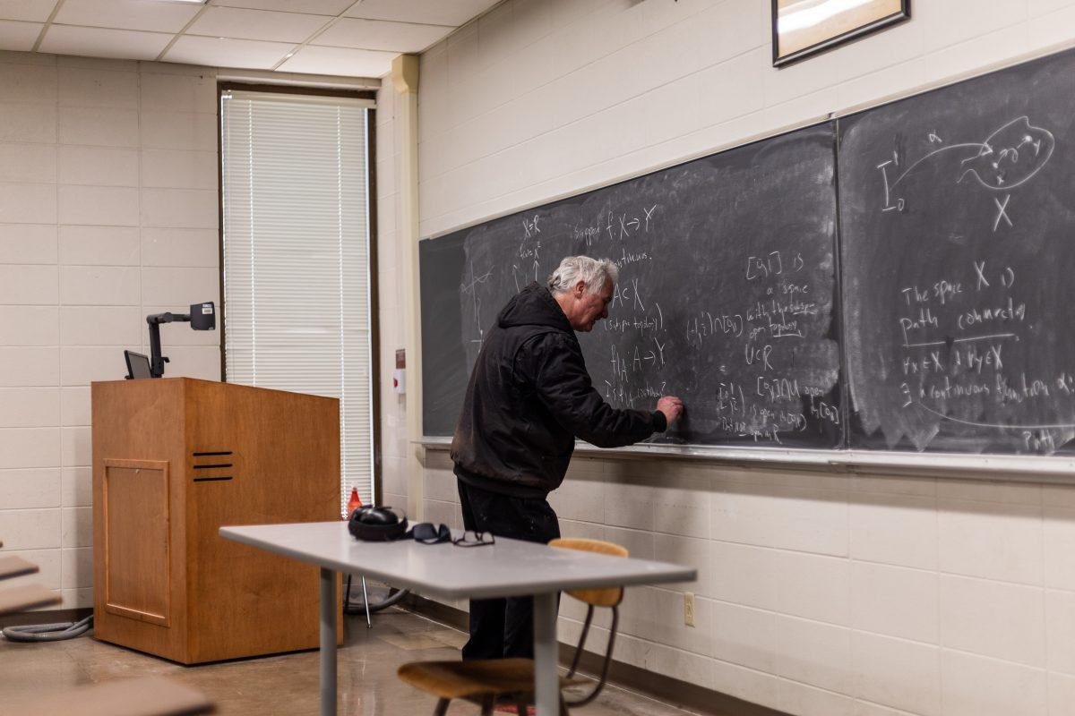 A professor writes equations on a chalkboard in Allen Hall while teaching.