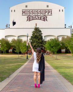 A graduate celebrates her upcoming graduation at Mississippi State University by tossing her graduation cap into the air in front of Davis Wade Stadium at The Junction. 