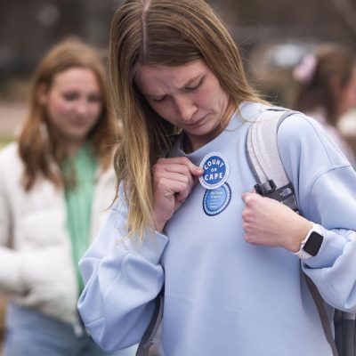 As the weather remains chilly Tuesday morning, a student places a "Count on Cape" sticker on her shirt for treasurer candidate Cape Merrell.